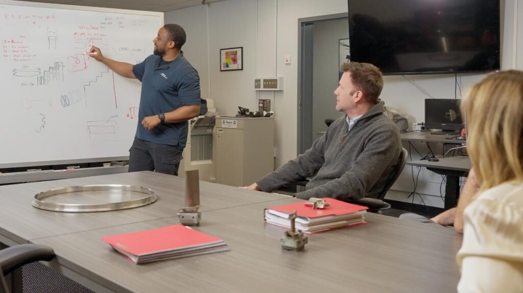 Burke Aerospace team members in a meeting room with one person writing on a whiteboard and others seated at a table.