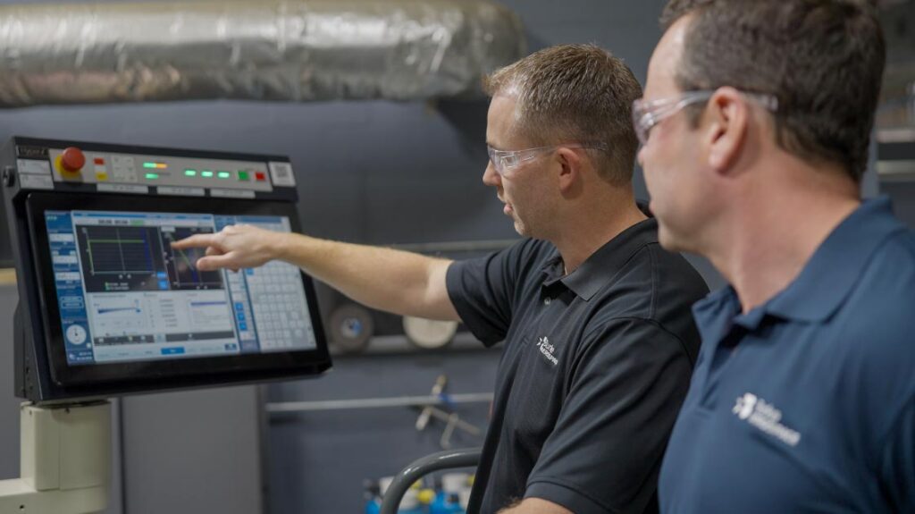 Burke Aerospace technicians in safety glasses and company shirts discussing precision machining operations at a work station in the aerospace manufacturing facility.